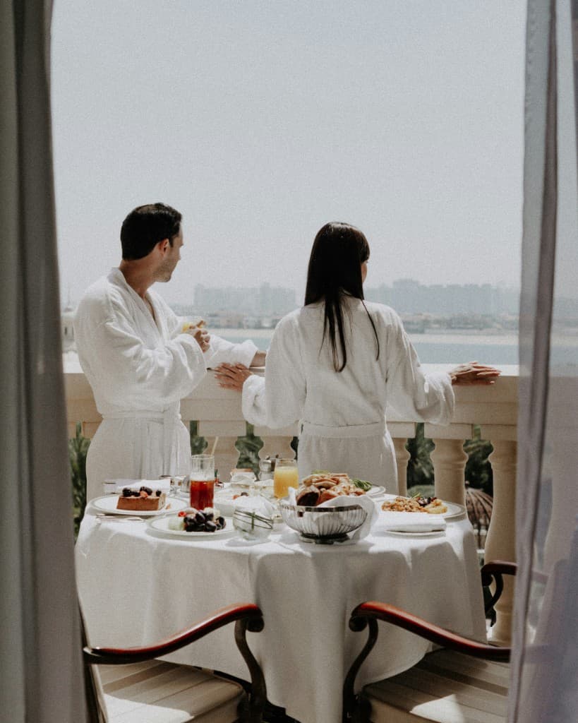 Couple in hotel bathrobes on a balcony with breakfast overlooking the water